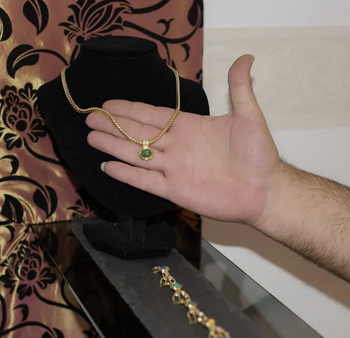 Goldschmied zeigt einen Goldanhänger mit Edelstein bei der Beratung